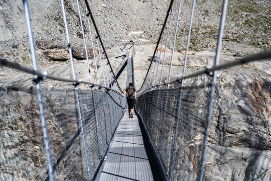 Female hiker walking on the hanging bridge over the Glacier de Corbassiere on a mountain trail around Valais Swiss Alps.