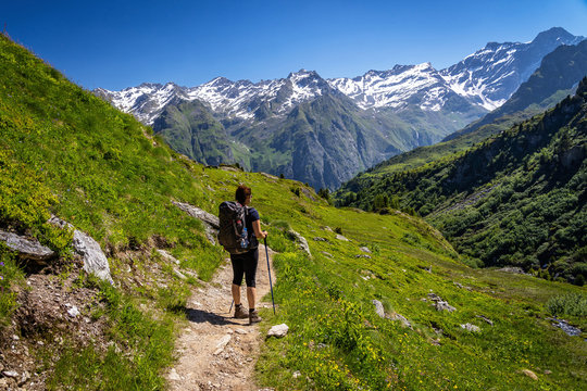 Female traveler with backpack hiking mountain trail and admiring views of Swiss Alps in Val de Bagnes area, Switzerland.