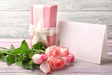 Beautiful roses, gift box and greeting card on wooden table
