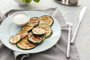 Plate with tasty grilled zucchini on light wooden table