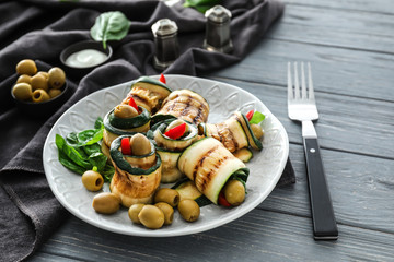 Plate with tasty zucchini rolls and green olives on wooden table