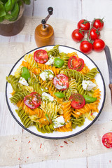 Italian food - Salad with colorful pasta, cherry tomatoes, feta cheese and fresh basil on white wooden background