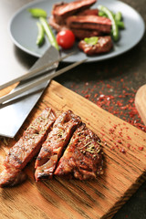 Wooden board with cut grilled steak on table