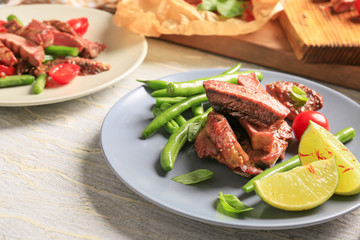 Plate with cut grilled steak and vegetables on wooden table
