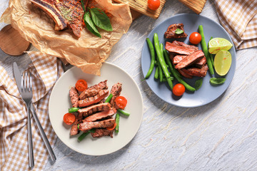 Plates with cut grilled steaks and vegetables on wooden table
