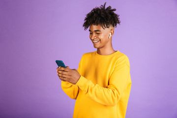 Portrait of african american man smiling and holding smartphone, wearing bluetooth earphone,...