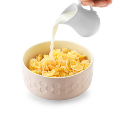 Pouring of milk into bowl with healthy cornflakes on white background