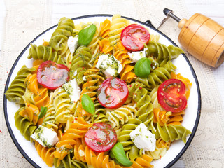 Kuchnia włoska - Sałatka z kolorowego makaronu, pomidorów koktajlowych, sera feta i świeżej bazylii na białym drewnianym tle. © czarny_bez
