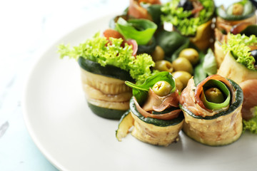 Tasty zucchini rolls with prosciutto on plate, closeup
