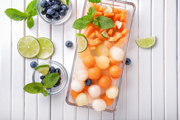 Plate with delicious melon balls and berries on white wooden table