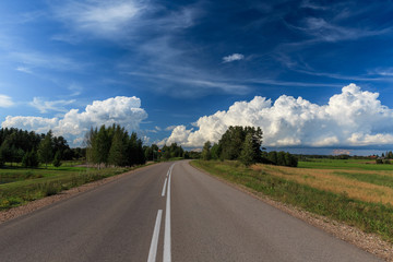 Road up hill with green grass field under white clouds and blue sky in summer day. Latgale. Latvia