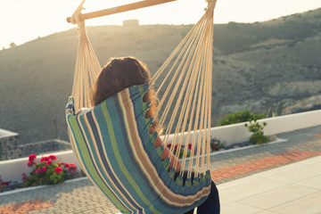 A girl is resting in the gammack in her villa in the garden at sunset