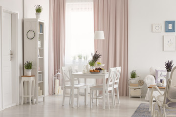 White flat interior with window with curtains, fresh lavender, dining table with breakfast and posters on wall in the real photo
