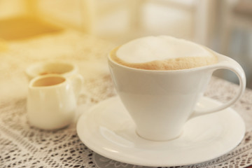 Confectioners atmosphere concept in vintage toned color. Cup of cappuccino coffee on wooden table with warm light flare.