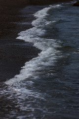 The surf wave line on a dark pebble beach in the evening