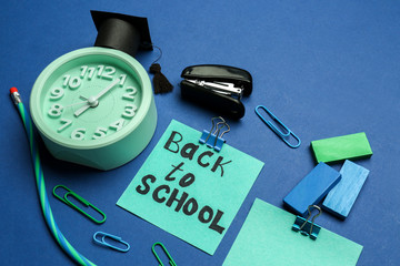 Sheet of paper with phrase BACK TO SCHOOL and stationery on color background