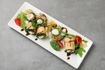 Plate with tasty zucchini rolls on grey background
