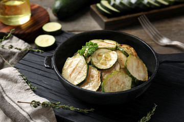 Pan with tasty grilled zucchini on wooden board