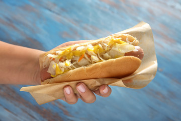 Woman holding tasty hot dog with sauerkraut on color background