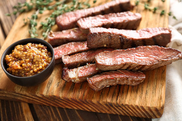 Cut grilled steak with mustard sauce on wooden board