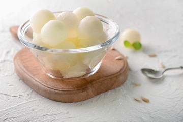 Bowl with tasty melon balls on wooden board