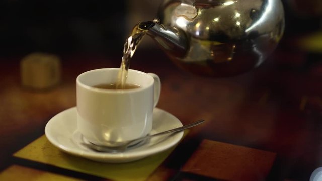 Hot tea flows in a glass from a teapot