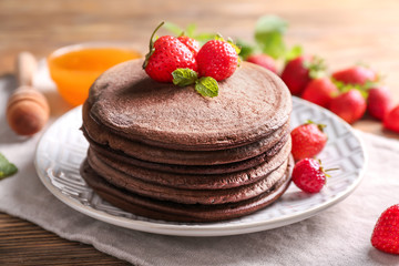 Tasty chocolate pancakes with strawberries on plate