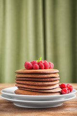 Plate with stack of tasty chocolate pancakes and raspberries on wooden table