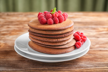 Plate with stack of tasty chocolate pancakes and raspberries on wooden table