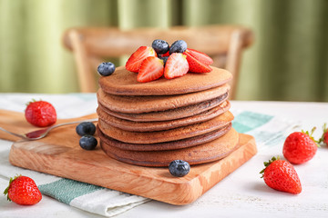 Wooden board with stack of tasty chocolate pancakes and berries on light table