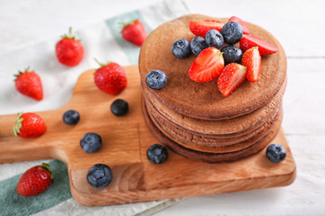 Wooden board with stack of tasty chocolate pancakes and berries on light table