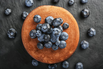 Tasty chocolate pancakes with blueberries on dark table, top view