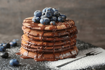 Tasty chocolate pancakes with sweet sauce and blueberries on slate plate