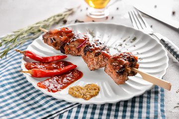 Plate with delicious shish kebab and sauce on table