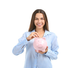 Young woman putting money into piggy bank on white background