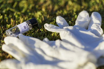 Illustration with mock up of Novichok agent (A-234) bottle and white rubber gloves on grass. Fictitious title on bottle in Russian: Novichok