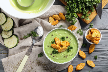 Bowl with tasty zucchini soup and croutons on wooden table