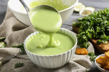 Pouring of zucchini soup from ladle into bowl on table