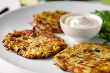 Tasty zucchini pancakes with sauce on plate, closeup