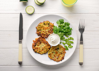 Plate with zucchini pancakes and sauce on light wooden table
