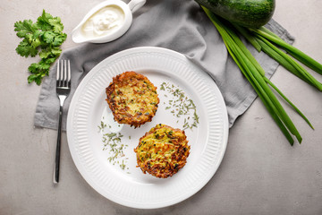 Plate with zucchini pancakes and sauce on grey table
