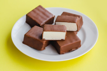 Chocolate sweets with white souffle on a plate on a yellow background.