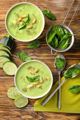 Bowls with delicious zucchini soup and herbs on wooden table
