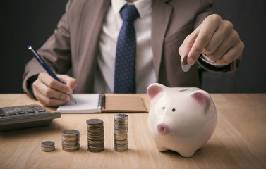 Businessman accountant holding coin putting in piggy bank. concept saving money for finance accounting.