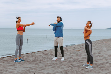 Group of young people is warming up before jogging on the beach by the sea
