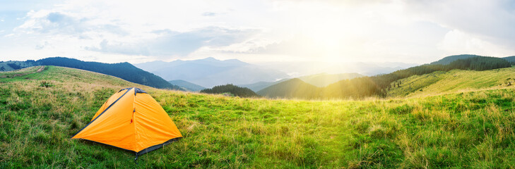 Orange tent on meadow with green grass in mountains under bright © alexlukin