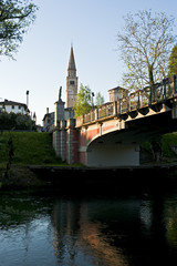 The Adam and Eve bridge over the Noncello river in Pordenone. In the background the bell tower of the Cathedral of San Marco. Italy.