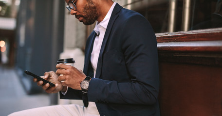 Businessman sitting outside with coffee using phone