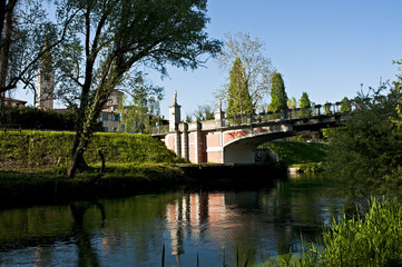 The Adam and Eve bridge over the Noncello river in Pordenone. In the background the bell tower of the Cathedral of San Marco. Italy.