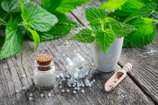 Nettle healing herbs, mortar and bottles of homeopathic globules.